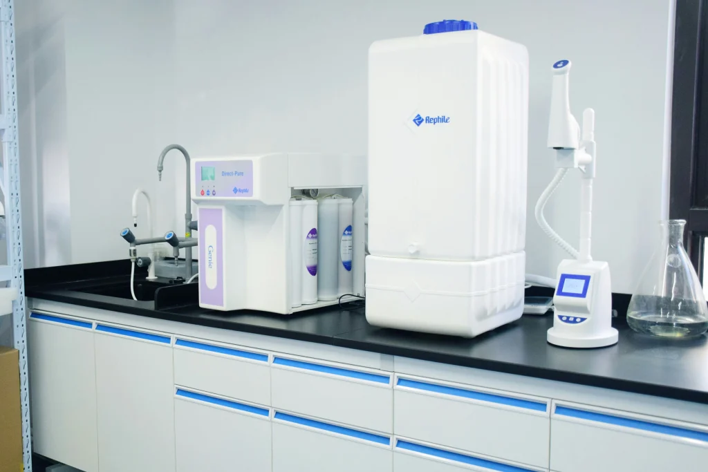A laboratory countertop with water purification equipment, including a UV municipal waste water treatment system, a filtration unit, a white water tank, digital dispenser, faucet, and glass flask.