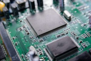 Close-up of a Printed Circuit Board featuring several black integrated circuits, microchips, and various electronic components interconnected by fine silver traces.